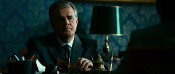 Movie still from “Transporter 3” (2008), directed by Olivier Megaton – An older man sitting at a table in a suit and tie; Close Up shot, Over the shoulder angle