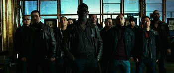 Movie still from “Transporter 3” (2008), directed by Olivier Megaton – A group of men standing next to each other in front of a window; Medium shot, Low angle