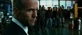 Movie still from “Transporter 3” (2008), directed by Olivier Megaton – A man in a suit and tie in front of a group of people; Close Up shot, Low angle