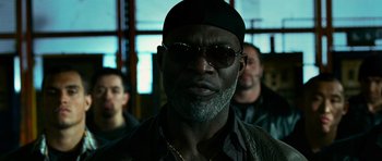 Movie still from “Transporter 3” (2008), directed by Olivier Megaton – A man with a beard wearing sunglasses and a black hat; Close Up shot, Low angle
