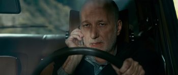 Movie still from “Transporter 3” (2008), directed by Olivier Megaton – A man sitting in the back seat of a car while talking on a cell phone; Close Up shot, Low angle