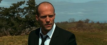 Movie still from “Transporter 3” (2008), directed by Olivier Megaton – A man wearing a suit and tie standing in front of a field; Close Up shot, Low angle