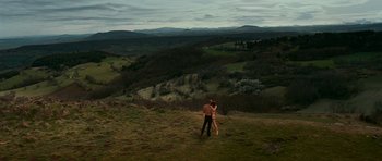 Movie still from “Transporter 3” (2008), directed by Olivier Megaton – A man and a woman standing on top of a grass covered hill; Extreme Wide shot, High angle