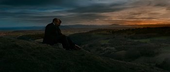 Movie still from “Transporter 3” (2008), directed by Olivier Megaton – A man sitting on top of a hill at sunset; Extreme Wide shot, Low angle