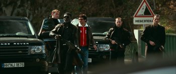 Movie still from “Transporter 3” (2008), directed by Olivier Megaton – A group of men standing next to each other on a street; Wide shot, Low angle