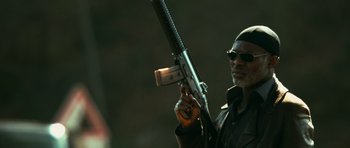 Movie still from “Transporter 3” (2008), directed by Olivier Megaton – A man holding a gun while wearing sunglasses; Close Up shot, Low angle