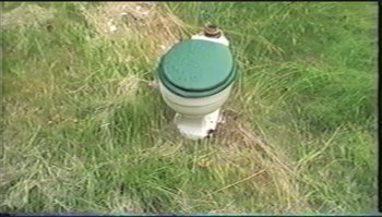 Movie still from “Trash Humpers” (2009), directed by Harmony Korine – A toilet sitting in the middle of a grassy field; Extreme Close Up shot, Overhead angle