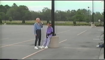 Movie still from “Trash Humpers” (2009), directed by Harmony Korine – Two people standing in a parking lot next to a light pole; Wide shot, High angle