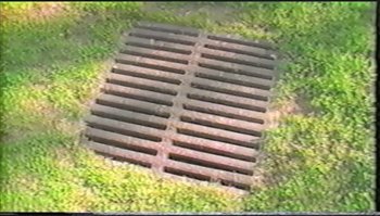 Movie still from “Trash Humpers” (2009), directed by Harmony Korine – An aerial view of a metal grate in the middle of a grass field; Extreme Wide shot, Overhead angle