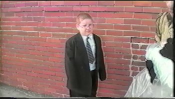 Movie still from “Trash Humpers” (2009), directed by Harmony Korine – A boy in a suit and tie standing in front of a brick wall; Wide shot, High angle