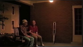 Movie still from “Trash Humpers” (2009), directed by Harmony Korine – Two men sitting on a bench in front of a brick wall; Wide shot, High angle