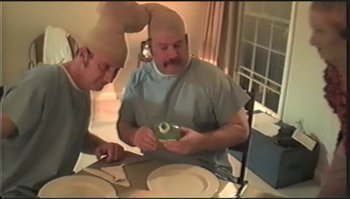Movie still from “Trash Humpers” (2009), directed by Harmony Korine – Two men sitting at a table with a plate of food; Medium shot, High angle