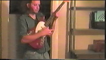 Movie still from “Trash Humpers” (2009), directed by Harmony Korine – A man holding a guitar in front of a window; Medium shot, High angle