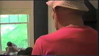 Movie still from “Trash Humpers” (2009), directed by Harmony Korine – A person wearing a hat and a red shirt; Medium shot, Over the shoulder angle