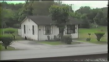 Movie still from “Trash Humpers” (2009), directed by Harmony Korine – A small white house sitting on the side of a road; Extreme Wide shot, High angle