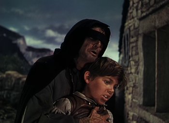 Movie still from “Treasure Island” (1950), directed by Byron Haskin – A man and a boy are standing next to each other; Medium shot, High angle