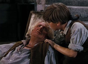 Movie still from “Treasure Island” (1950), directed by Byron Haskin – An older man and a young boy laying on the ground; Close Up shot, Over the shoulder angle