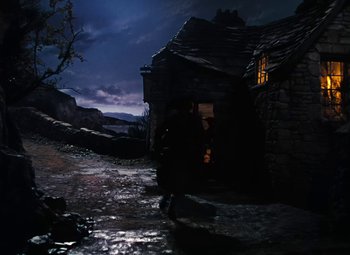 Movie still from “Treasure Island” (1950), directed by Byron Haskin – A dark scene of a house with a window lit by a lamp; Extreme Wide shot, High angle