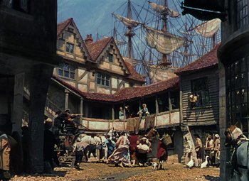 Movie still from “Treasure Island” (1950), directed by Byron Haskin – A group of people standing in a courtyard next to a building; Extreme Wide shot, High angle