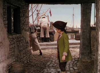 Movie still from “Treasure Island” (1950), directed by Byron Haskin – A young boy dressed as a pirate standing in front of a boat; Wide shot, High angle