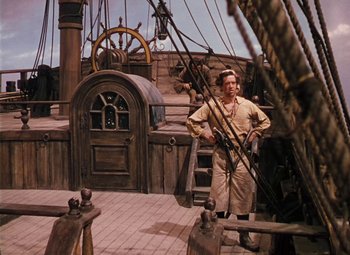 Movie still from “Treasure Island” (1950), directed by Byron Haskin – A man standing on top of a boat in a dock; Wide shot, High angle