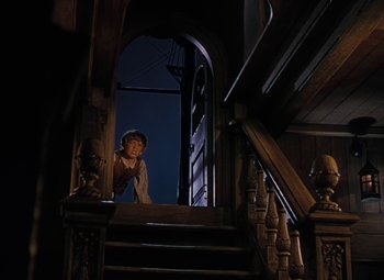 Movie still from “Treasure Island” (1950), directed by Byron Haskin – A woman standing on a staircase looking out a window; Wide shot, Low angle