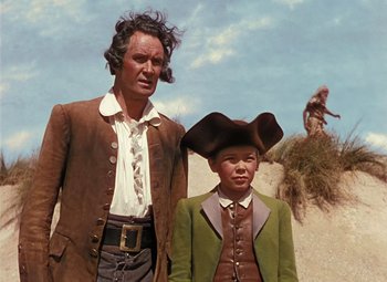 Movie still from “Treasure Island” (1950), directed by Byron Haskin – A man standing next to a young boy wearing a pirate hat; Medium shot, Low angle