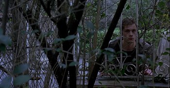 Movie still from “Trouble Every Day” (2001), directed by Claire Denis – A man looking out of a window through a fence; Medium shot, Over the shoulder angle