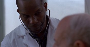 Movie still from “Trouble Every Day” (2001), directed by Claire Denis – A man wearing a white lab coat and stethoscope looking at another man; Close Up shot, Low angle
