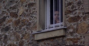 Movie still from “Trouble Every Day” (2001), directed by Claire Denis – A person looking out of a window through bars; Medium shot, Low angle
