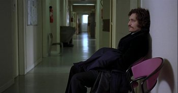 Movie still from “Trouble Every Day” (2001), directed by Claire Denis – A man sitting in a chair in a hospital hallway; Medium shot, High angle