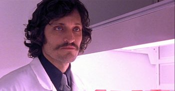 Movie still from “Trouble Every Day” (2001), directed by Claire Denis – A man with long black hair wearing a white lab coat; Close Up shot, Low angle