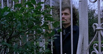 Movie still from “Trouble Every Day” (2001), directed by Claire Denis – A man standing next to a tree looking out of a fence; Close Up shot, Low angle