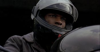 Movie still from “Trouble Every Day” (2001), directed by Claire Denis – A man wearing a motorcycle helmet while standing in a parking lot; Close Up shot, Low angle