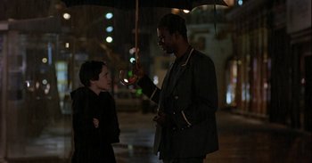 Movie still from “Trouble Every Day” (2001), directed by Claire Denis – A man holding an umbrella talking to a young boy; Medium shot, Over the shoulder angle