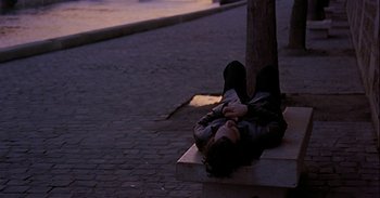 Movie still from “Trouble Every Day” (2001), directed by Claire Denis – A person laying on the ground near a tree; Wide shot, High angle