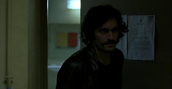 Movie still from “Trouble Every Day” (2001), directed by Claire Denis – A man in a leather jacket standing next to a wall; Close Up shot, Over the shoulder angle
