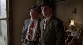 Movie still from “True Confessions” (1981), directed by Ulu Grosbard – A couple of men standing next to each other wearing suits; Medium shot, Low angle