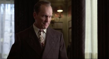 Movie still from “True Confessions” (1981), directed by Ulu Grosbard – A man in a suit and tie standing next to a wall; Medium shot, Low angle