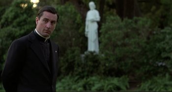 Movie still from “True Confessions” (1981), directed by Ulu Grosbard – A man standing in front of a statue in a garden; Medium shot, Low angle