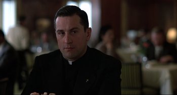 Movie still from “True Confessions” (1981), directed by Ulu Grosbard – A man wearing a priest's outfit sitting in a restaurant; Close Up shot, Low angle