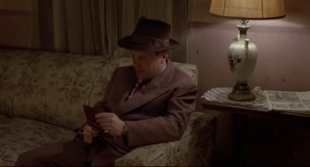 Movie still from “True Confessions” (1981), directed by Ulu Grosbard – A man sitting on top of a couch in a living room; Medium shot, High angle
