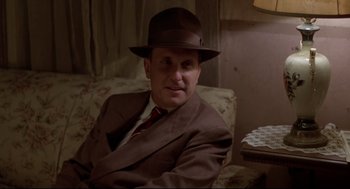 Movie still from “True Confessions” (1981), directed by Ulu Grosbard – A man in a suit and hat sitting on a couch; Close Up shot, Low angle