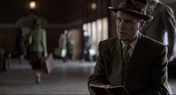 Movie still from “True Confessions” (1981), directed by Ulu Grosbard – A man in a suit and a hat is holding a book; Medium shot, Low angle