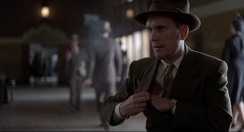 Movie still from “True Confessions” (1981), directed by Ulu Grosbard – A man in a suit and hat putting on a tie; Medium shot, Over the shoulder angle