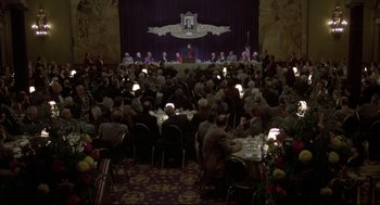 Movie still from “True Confessions” (1981), directed by Ulu Grosbard – A large group of people sitting at tables in a room; Extreme Wide shot, High angle