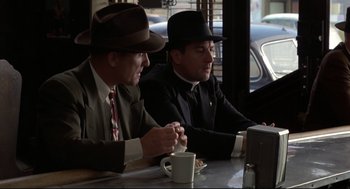 Movie still from “True Confessions” (1981), directed by Ulu Grosbard – A couple of men sitting at a table with a cup of coffee; Medium shot, Over the shoulder angle