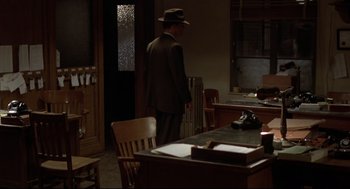 Movie still from “True Confessions” (1981), directed by Ulu Grosbard – A man in a suit and hat standing in front of a desk; Wide shot, High angle