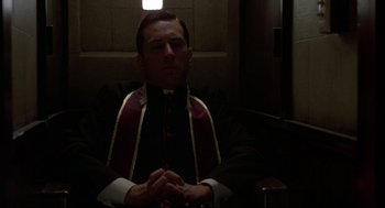 Movie still from “True Confessions” (1981), directed by Ulu Grosbard – A man sitting in a dark room wearing a priest's outfit; Medium shot, Low angle