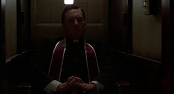 Movie still from “True Confessions” (1981), directed by Ulu Grosbard – A man in a priest's outfit sitting in the dark; Medium shot, Low angle